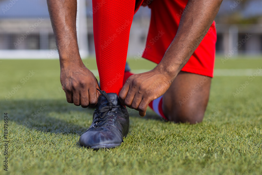 African American young male athlete tying shoelaces on soccer field outdoors