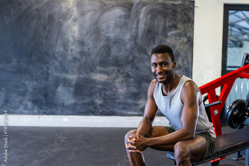 African American young male athlete sitting on a bench in a gym  smiling  copy space