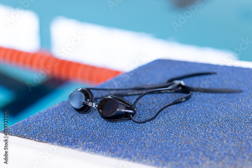 Swimming goggles resting on edge of indoor pool, close-up view, copy space