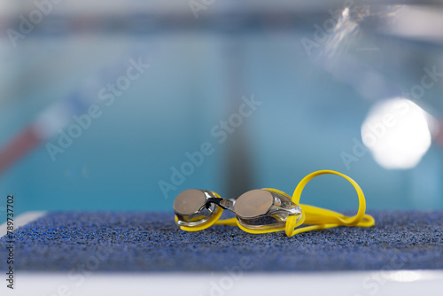 Swimming goggles resting on edge of pool indoors, clear water reflecting light, copy space