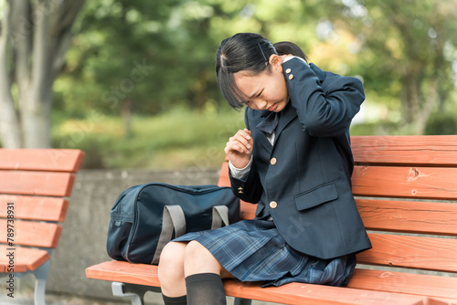 登校・下校中に首・肩を痛めて公園のベンチに座る中学生・高校生の女子生徒  © buritora