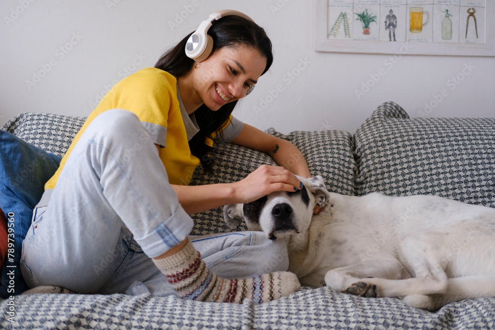 Smiling Woman at home using headphones bonding with dog Smiling Woman at home using headphones bonding with dog