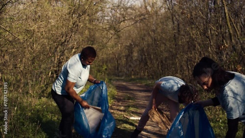 Diverse volunteers collecting garbage and junk from the forest area, fighting environmental pollution and conservation. Group of activists cleaning up the woods, recycling plastic waste. Camera B.