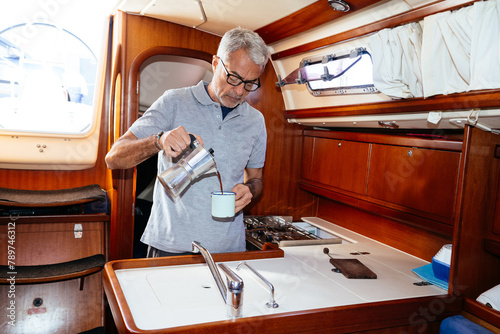 Elderly man pouring coffee into cup in cabin of yacht photo