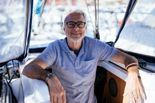 Positive senior man sitting in yacht by glass windshield on sunny day photo