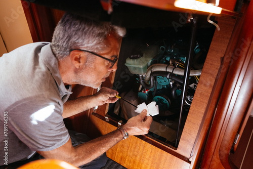 Elderly male technician checking oil of yacht engine photo