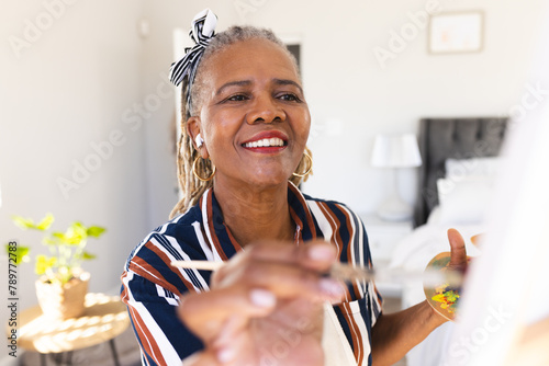 A senior African American woman is painting on canvas at home, smiling joyfully photo
