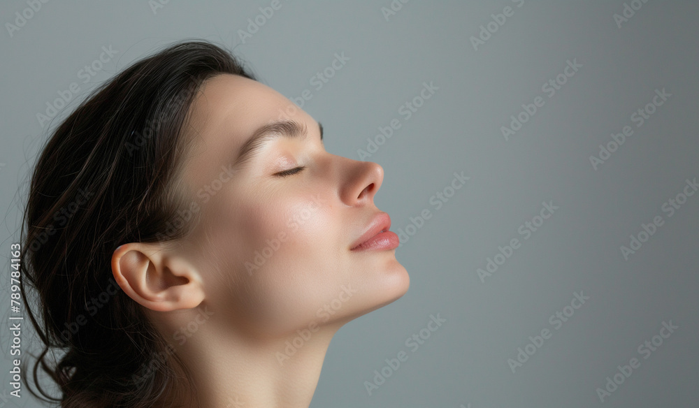 A profile view of a serene woman with eyes closed, her expression one of peace and introspection, set against a soft grey backdrop.