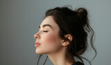 A woman in profile with closed eyes, exuding a sense of peace and tranquility against a muted gray backdrop.