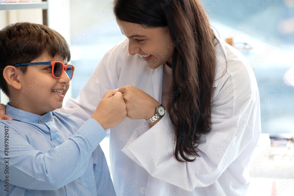 Indian child boy in traditional cloth trying out new eyeglasses with expert advice, bump their fist together, Asian boy holding and trying on new spectacles Indian child boy in traditional cloth trying out new eyeglasses with expert advice, bump their fist together, Asian boy holding and trying on new spectacles