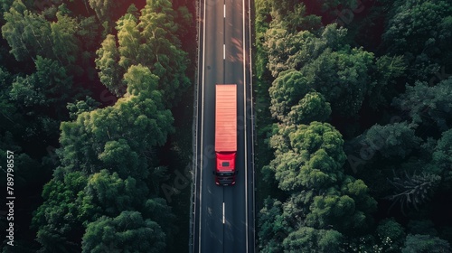 A red semi truck drives through a lush green forest on a winding road.