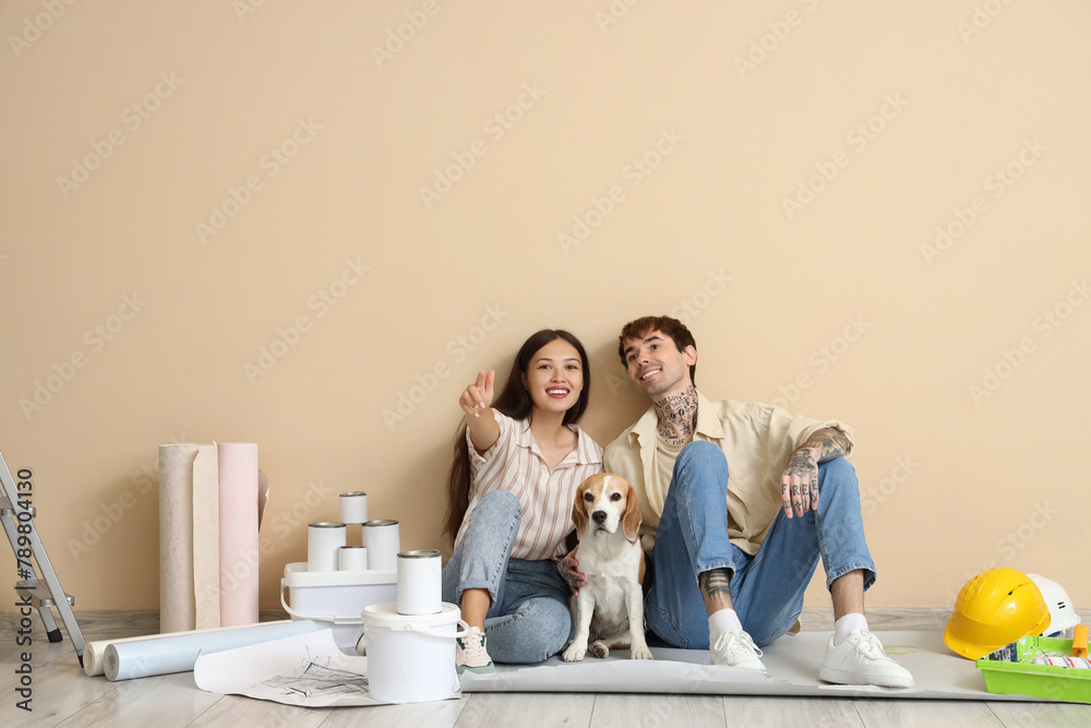 Young couple with Beagle dog and painting tools pointing at viewer during repair in their new house Young couple with Beagle dog and painting tools pointing at viewer during repair in their new house