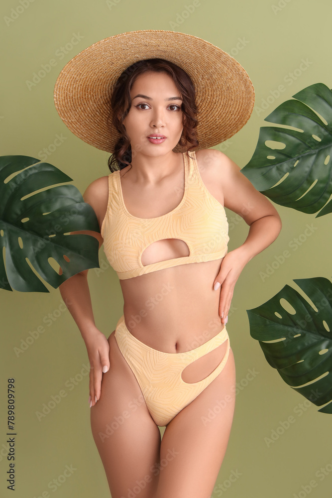 Obraz premium Sexy young woman in swimsuit and tropical leaves on green background