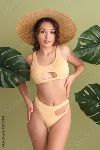 Sexy young woman in swimsuit and tropical leaves on green background
