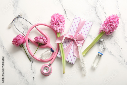 Stethoscope with ampules, gift box and flowers for International Nurses Day on white grunge background
