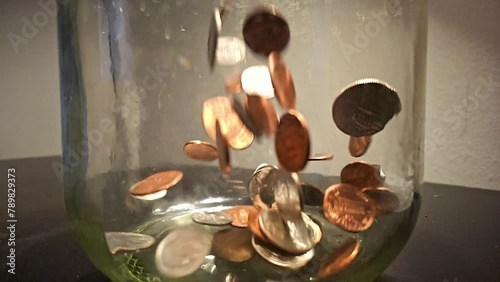 Super slow motion of coins dropping into a large mason jar photo