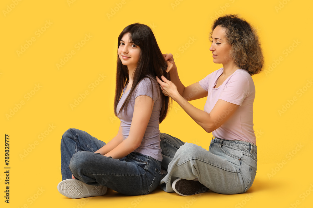 Beautiful mature woman brushing her teenage daughter's hair on yellow background. Mother's day Beautiful mature woman brushing her teenage daughter's hair on yellow background. Mother's day