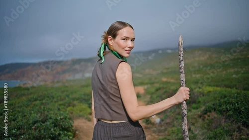 Outdoor woman going hill on summer day. Smiling hiker turning camera hold stick photo