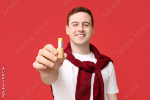 Happy young man with lip balm on red background