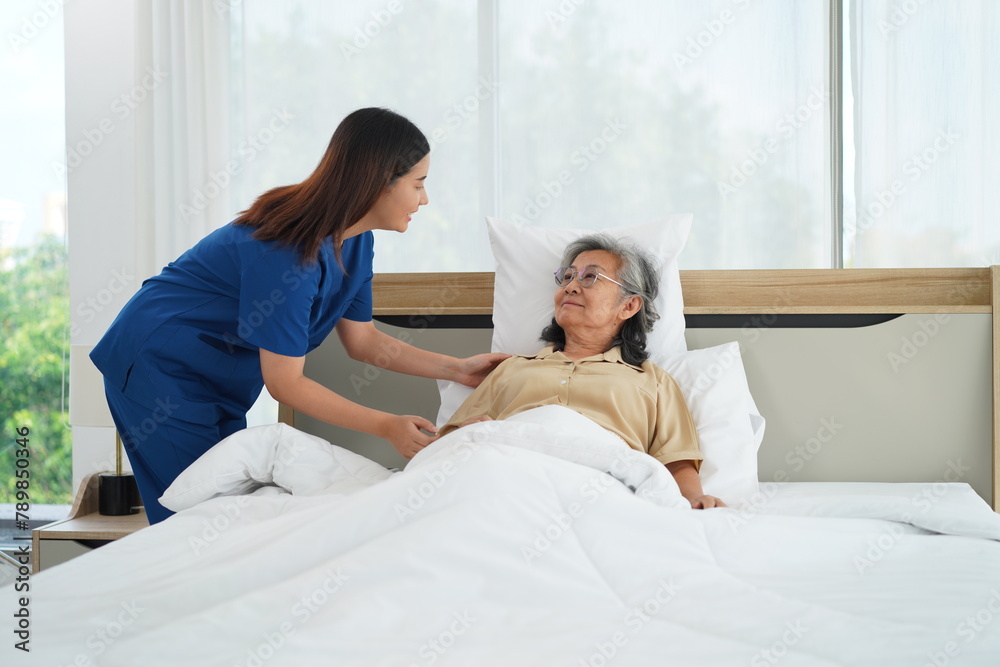Young Caregiver female take senior woman go to sleep on bed in bedroom Young Caregiver female take senior woman go to sleep on bed in bedroom