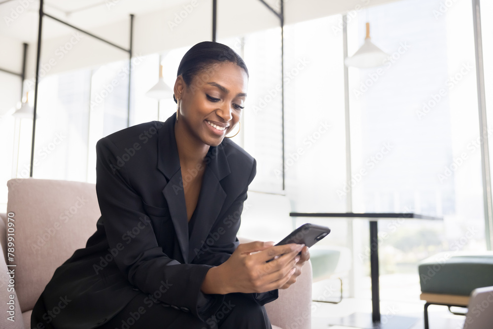 Positive beautiful Black business professional lady using application on cellphone for job communication, typing message on work chat, smiling, holding smartphone