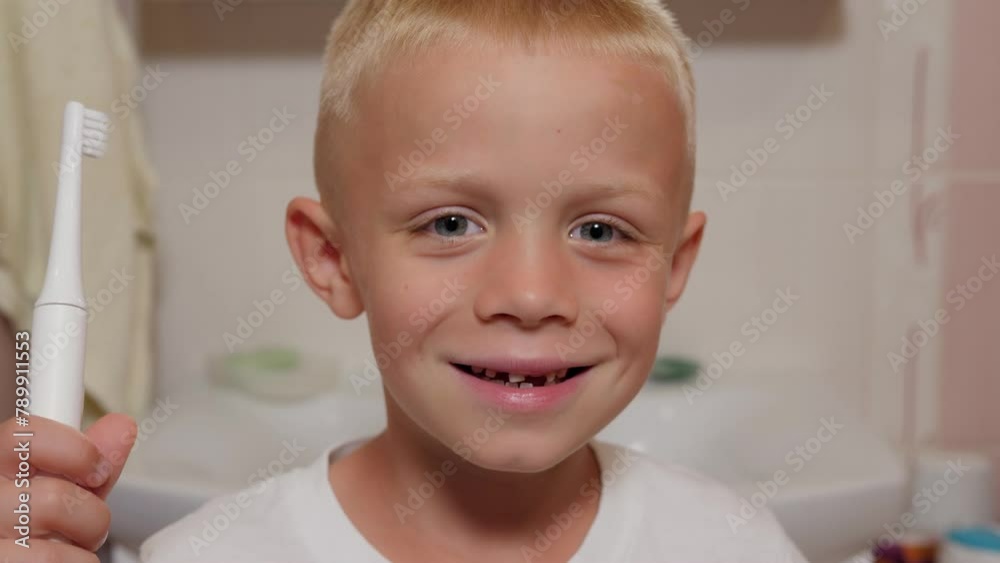 A little boy is standing in the bathroom with an electric toothbrush in his hands, his front baby teeth have fallen out. A little boy is standing in the bathroom with an electric toothbrush in his hands, his front baby teeth have fallen out.