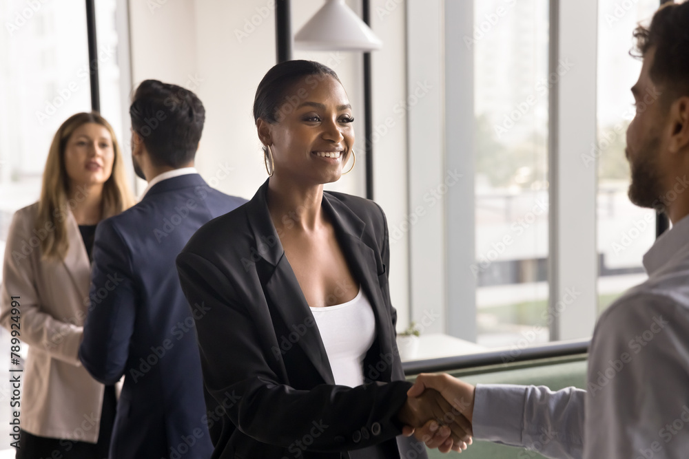 Happy beautiful African American businesswoman in formal suit shaking hands with company customer, male business partner, smiling, thanking for partnership, closing deal, getting agreement Happy beautiful African American businesswoman in formal suit shaking hands with company customer, male business partner, smiling, thanking for partnership, closing deal, getting agreement