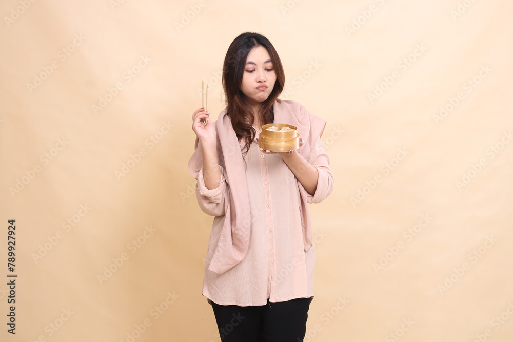 muslim girl indonesia pouting into dimsum and hand bringing chopsticks up and wooden bowl to center containing delicious dimsum muslim girl indonesia pouting into dimsum and hand bringing chopsticks up and wooden bowl to center containing delicious dimsum