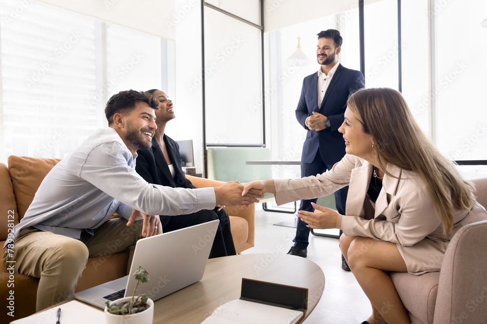 Fototapeta premium Cheerful business colleagues shaking hands at diverse business team meeting, sitting on couch, closing deal, getting agreement, enjoying successful teamwork, communication