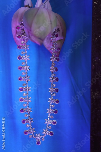 diamond studded 3  tier gold chain hanging from a lotus bud with chromo backdrop