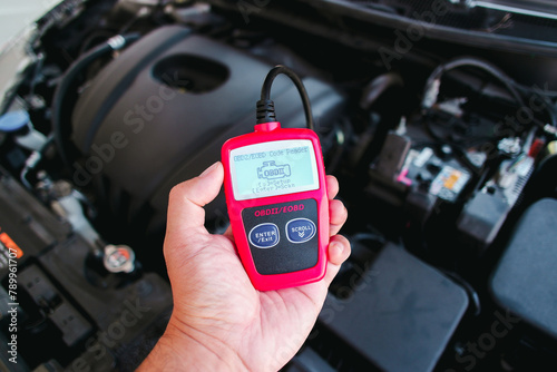 OBD2 or OBD scanner in a auto mechanic hand for engine system analysis with engine compartment blurred on background , Car maintenance service concept