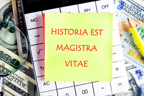 Historia est vitae magistra (History is the tutor of life) Latin phrase on the yellow sticker on the calculator on the background of dollars photo