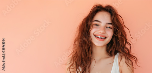 Young smiling girl with braces on a soft peach background. Copy space