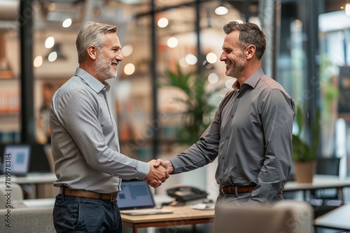 Two Smiling Businessmen Shaking Hands in a Modern Office Environment During the Daytime