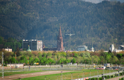 a light plane comes to land at the airfield against the backdrop of mountains and an old church