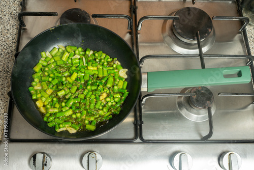 Fresh green asparagus diced and sizzling in a skillet on the stove.