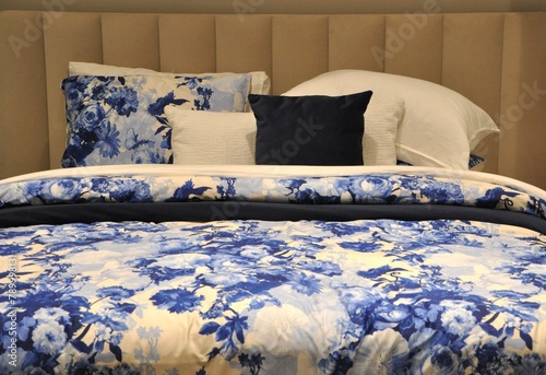 Beautiful beddings with blue and white floral design.Bed with blue floral sheets, white and blue pillows and Soft cushions and blanket.Blue bed furniture with patterned bed linen . Soft satin linen