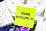 Latin quote Errare humanum est, meaning It is human nature to make mistakes. Mistakes are inherent in human existence. Text written on a yellow sticker near the calculator and the clock