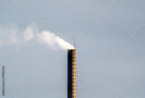 Smoke rises from chimney on building against blue sky