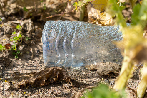Discarded plastic bottle with condensation among dry plants, highlighting environmental issues.