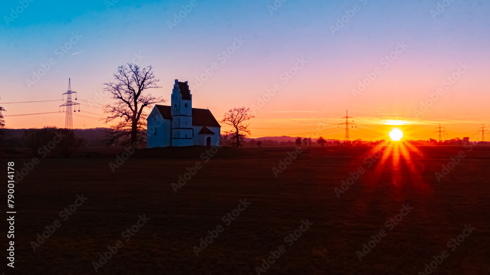 Fototapeta premium Sunset with a church silhouette and a sunstar at Huett, Eichendorf, Dingolfing-Landau, Bavaria, Germany