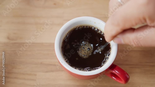 Top view of Person hand steering coffee in a cup with spoon. Breakfast morning of a cup hot black coffee on wooden background. footage b-roll Slow motion scene 4k. home making coffee.