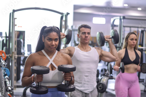 Group of multiracial people exercising their arms with dumbbells inside a gym, sport dress. Fitness and healthy lifestyle concept