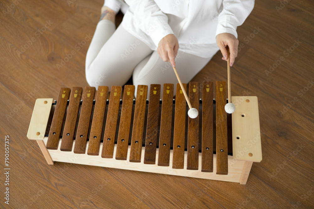 Beautiful young curly woman playing on a wooden xylophone sitting on the floor in white clothes