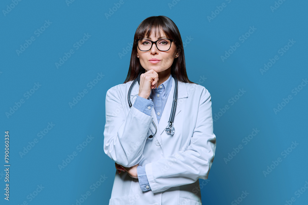 Confident serious female doctor looking at camera on blue background Confident serious female doctor looking at camera on blue background