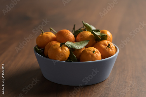 Small organic tangerines with leaves in ceramic bowl on wood table