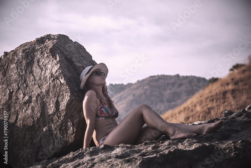 Beautiful girl on the stones by the sea. Sunny evening. Light at sunset. Girl in a bikini.