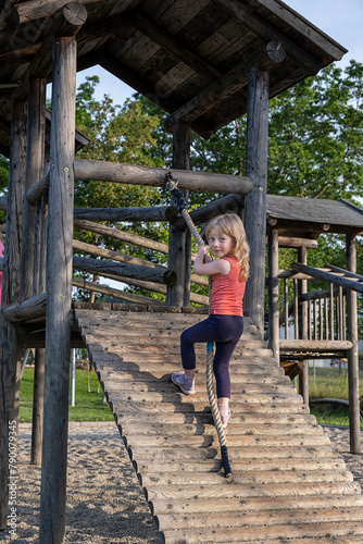 a little girl climbs a rope into a wooden castle on a summer playground