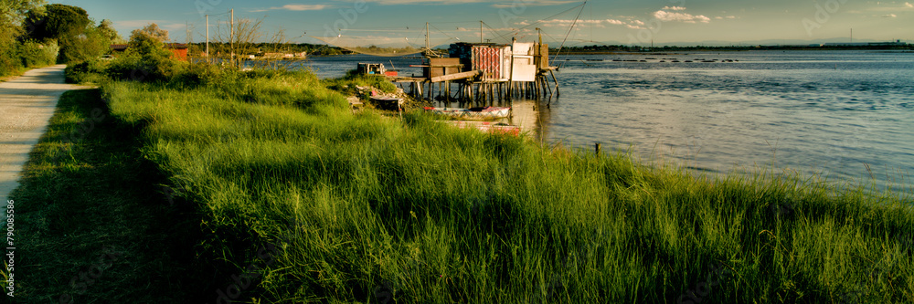 Tranquil waters embrace a picturesque scene of fishing boats and rustic huts along the shores of Pialassa dei Piomboni, near Ravenna Tranquil waters embrace a picturesque scene of fishing boats and rustic huts along the shores of Pialassa dei Piomboni, near Ravenna