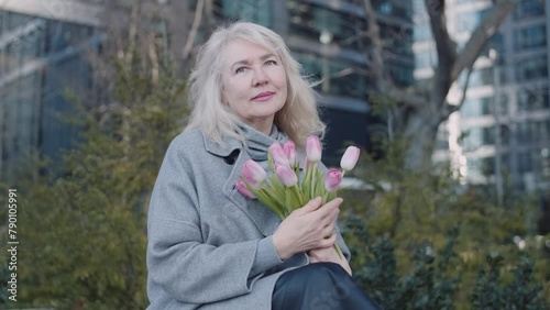 An elegant senior woman with tulips in a city yard